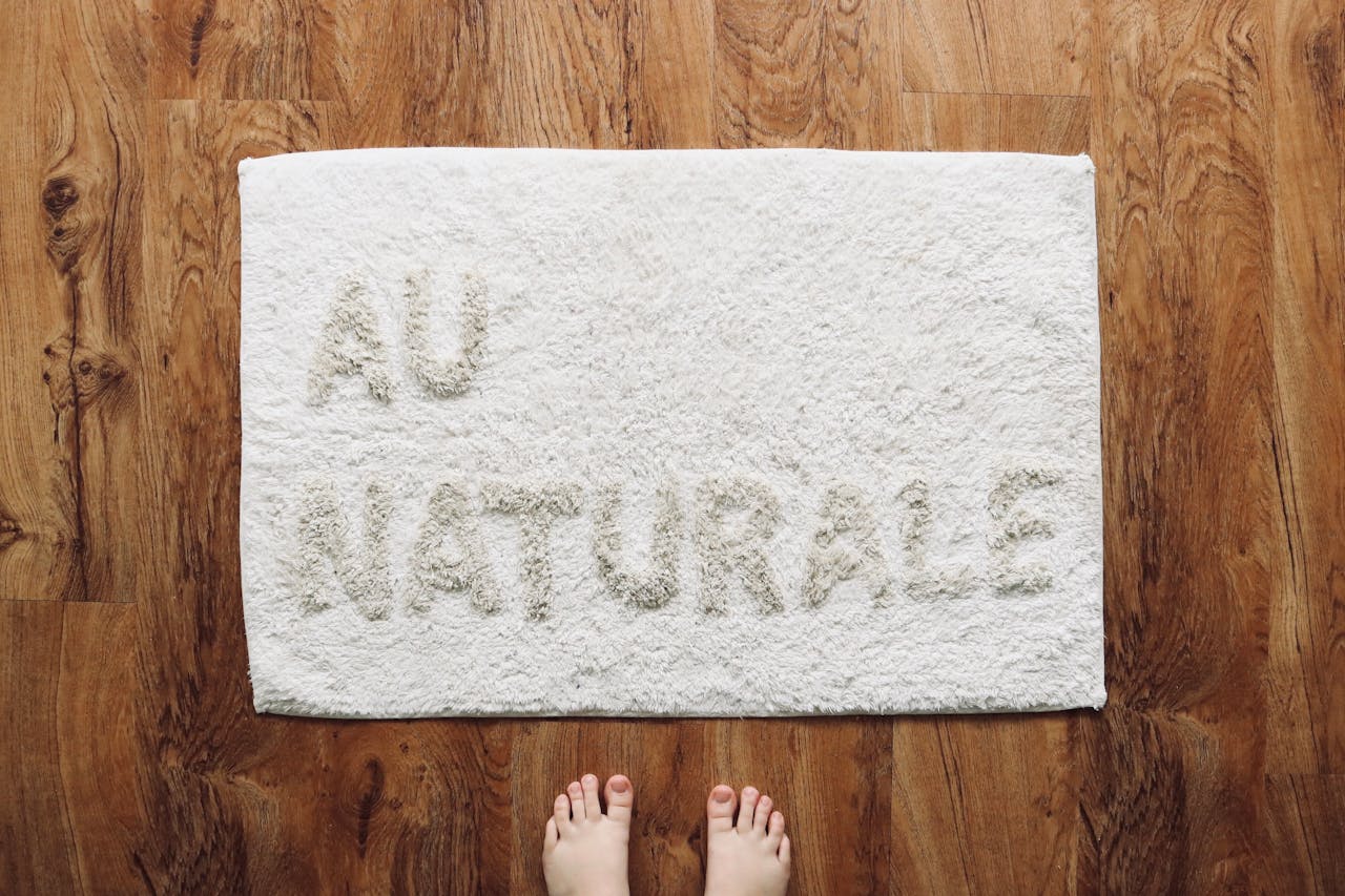 A white doormat with 'AU NATUREL' text on a wooden floor, viewed from above.